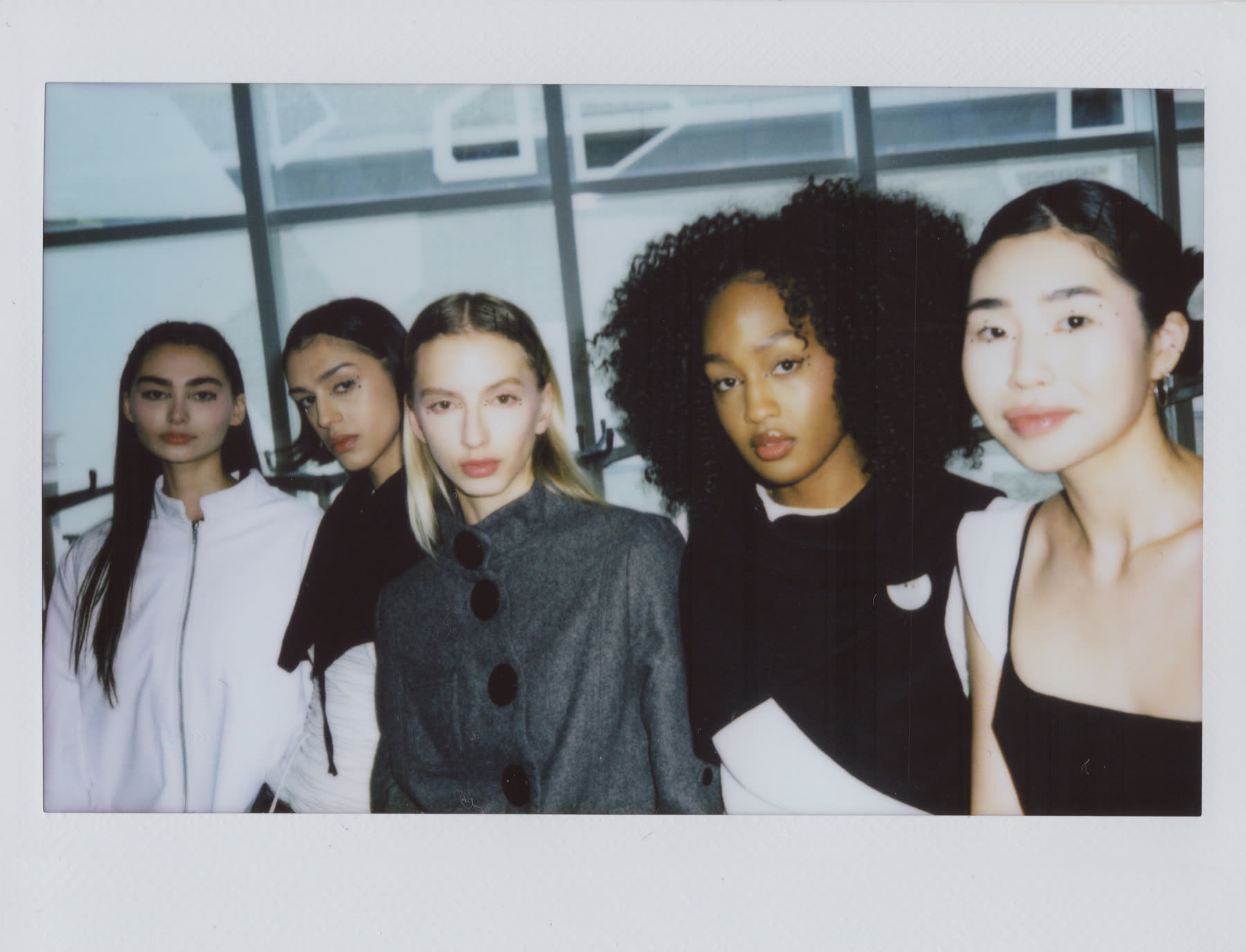 Instant photograph of the five models backstage before the show, in looks from the collection.